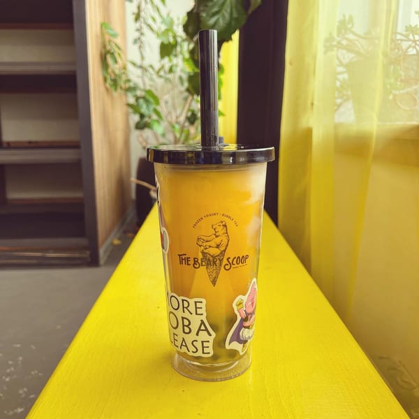 A Beary Scoop bubble tea with a black straw sits on a bright yellow surface.