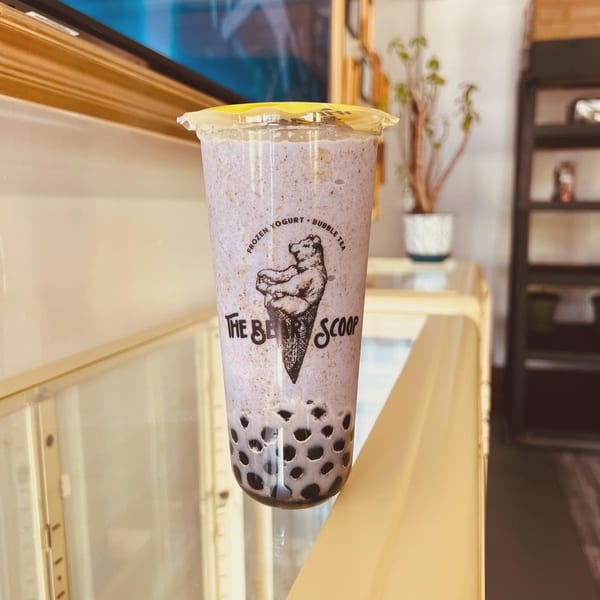 A purple bubble tea from The Beary Scoop, with a bear logo, sits on a counter.